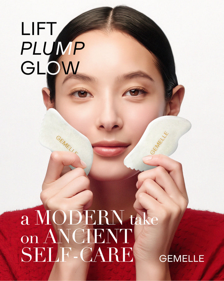 A GEMELLE Woman holding two White Jade Gua Sha tools with highlighting a modern take on ancient self-care, against a light background.